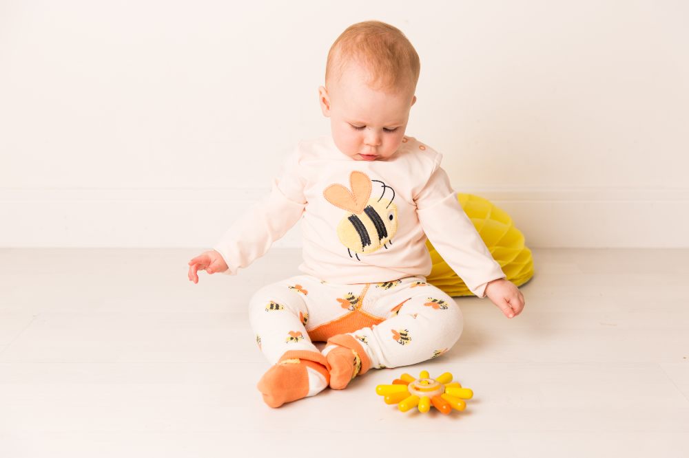 A baby sat on the floor wearing a top and leggings with Bumble Bees on 
