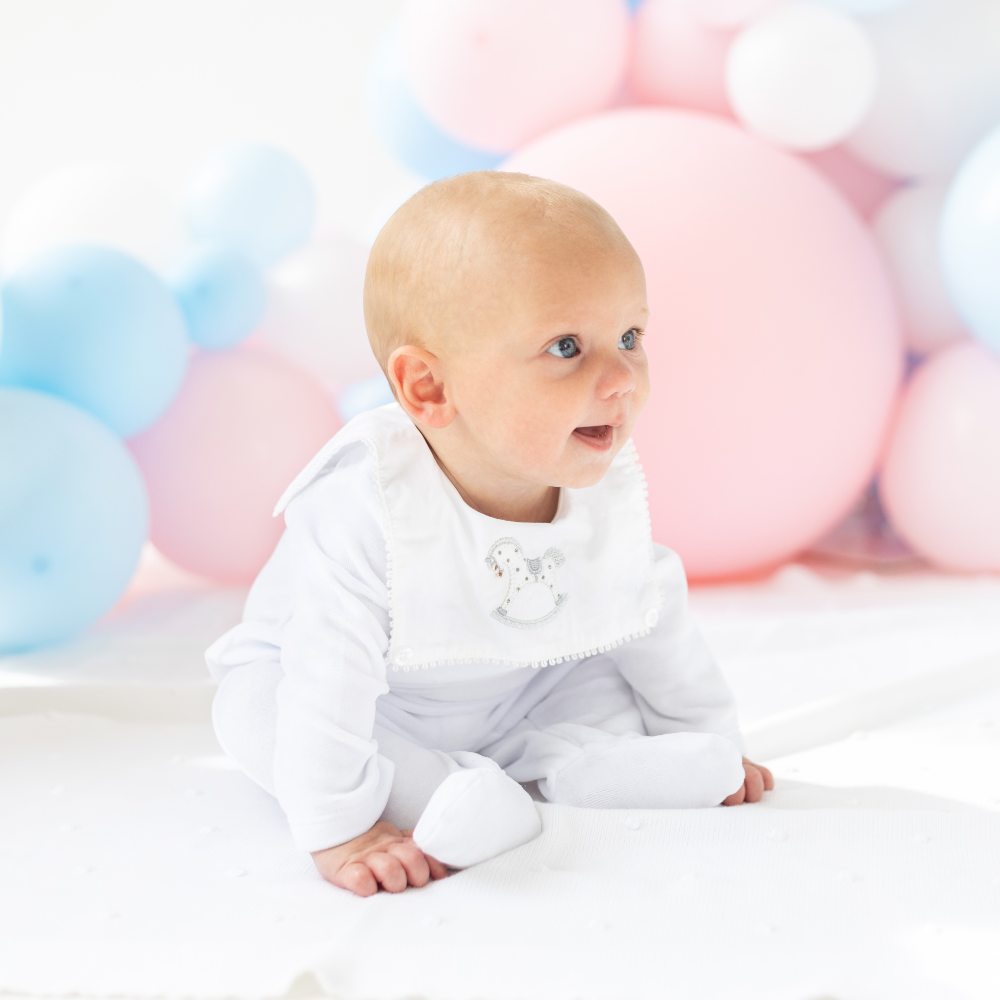 A baby sat on the floor in front on pink and blue balloons 