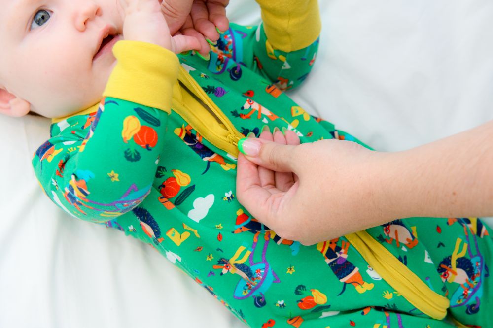 Someone zipping up a baby's green babygro by Ducky Zebra