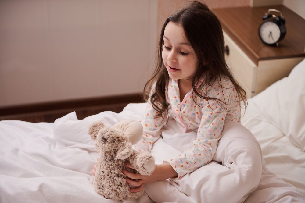A young child sitting in bed wearing pyjamas and holding a teddy bear 