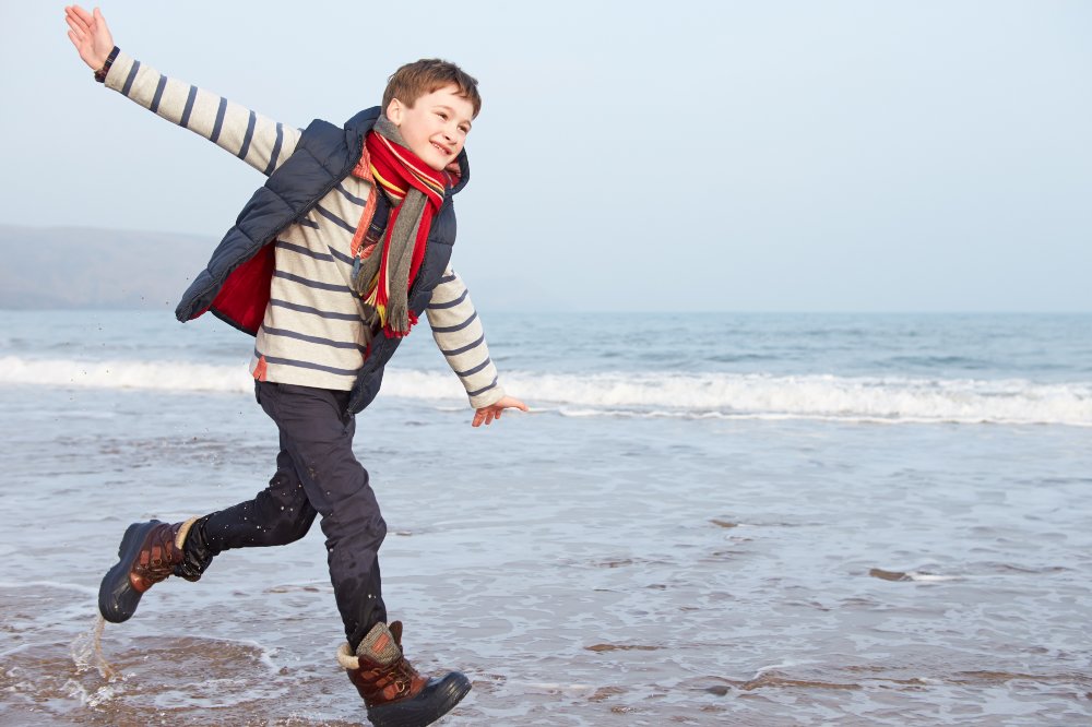 A boy running on a beach wearing winter clothes and a scarf 