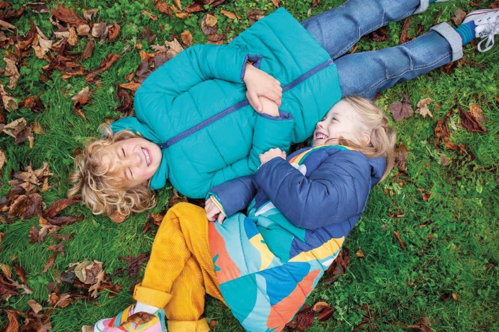 Two children lying on grass wearing winter coats