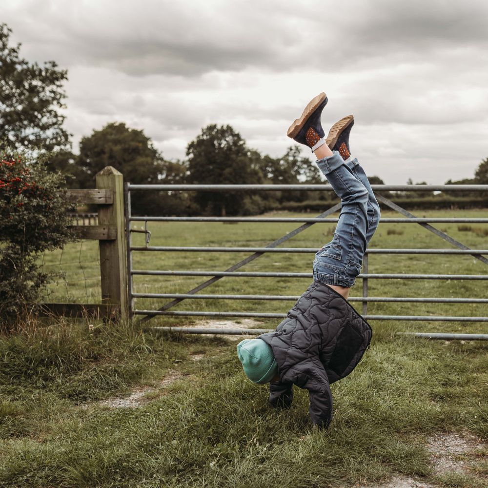 A young boy in a filed doing a handstand in front of a gate 