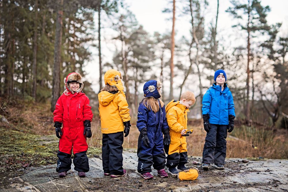 A group of children stood outside in a wood wearing hats and outerwear