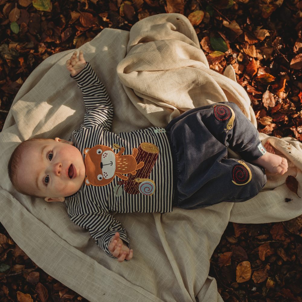 A baby lying on a rug on leaves wearing an outfit with animals on 