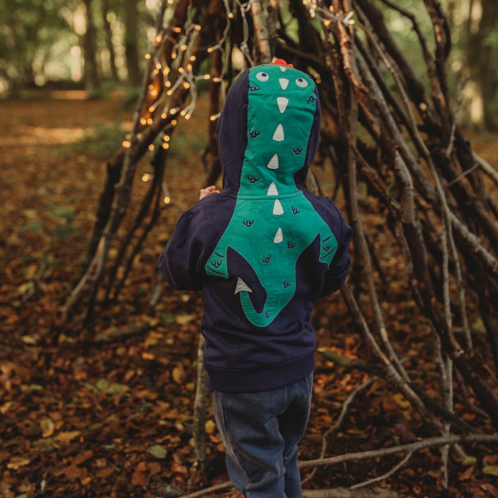 A child stood in a wood in front of a den wearing a blue hooded top with a dragon on the back
