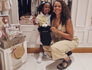 A young child and a woman holding a black baby outfit by Little Black Outfit in a childrenswear store