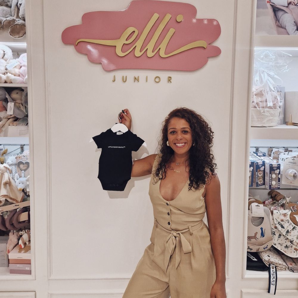 A woman holding up a black baby outfit by Little Black Outfit in the Elli Junior childrenswear store