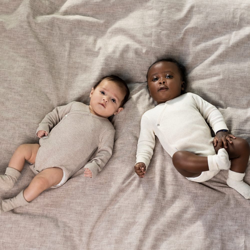 Two babies wearing babygros lying on bedding 