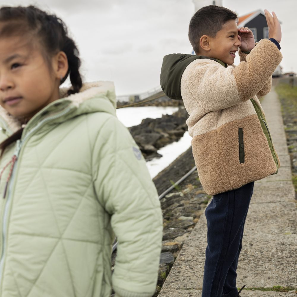 Two children stood outside wearing winter coats 