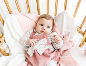A baby wearing a pink knitted outfit lying in a cot