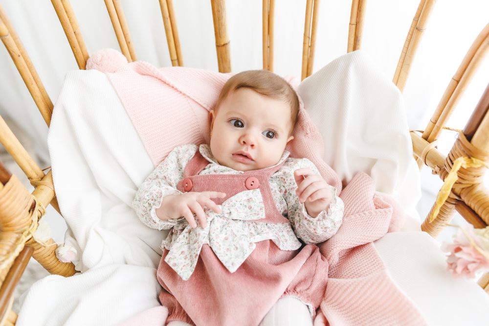 A baby wearing a pink knitted outfit lying in a cot