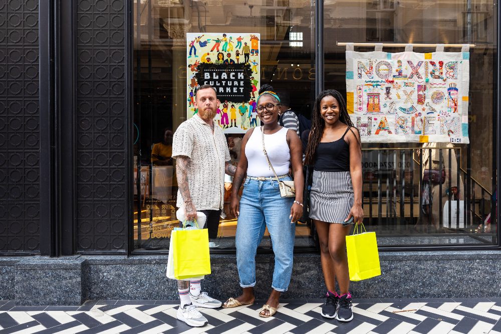 Three people stood outside a building holding yellow shopping bags