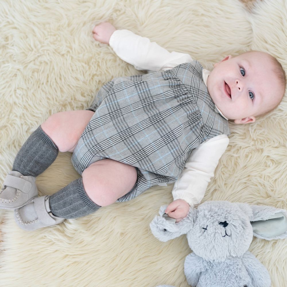 A young child lying on a rug wearing a grey babygro and holding a rabbit soft toy 