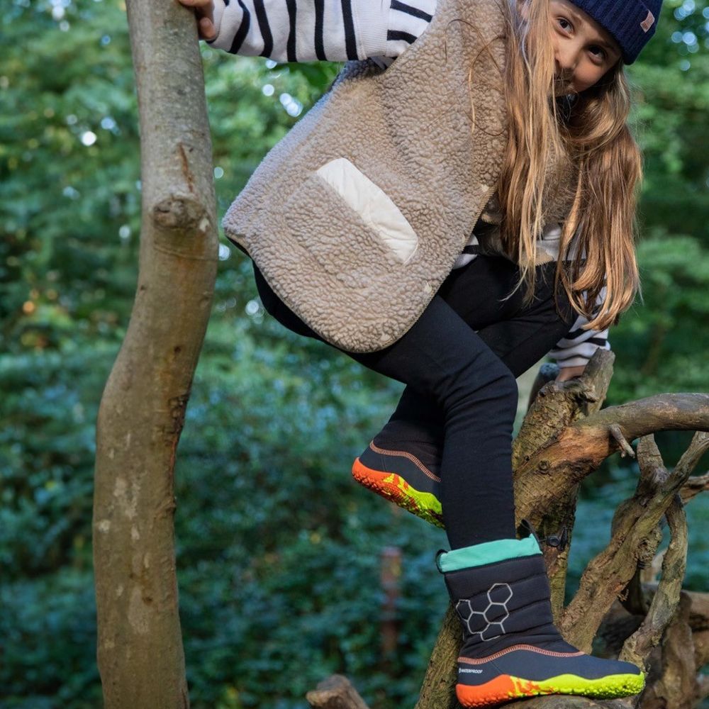 A girl climbing a tree wearing the LUMI Kids Boots by Vivobarefoot