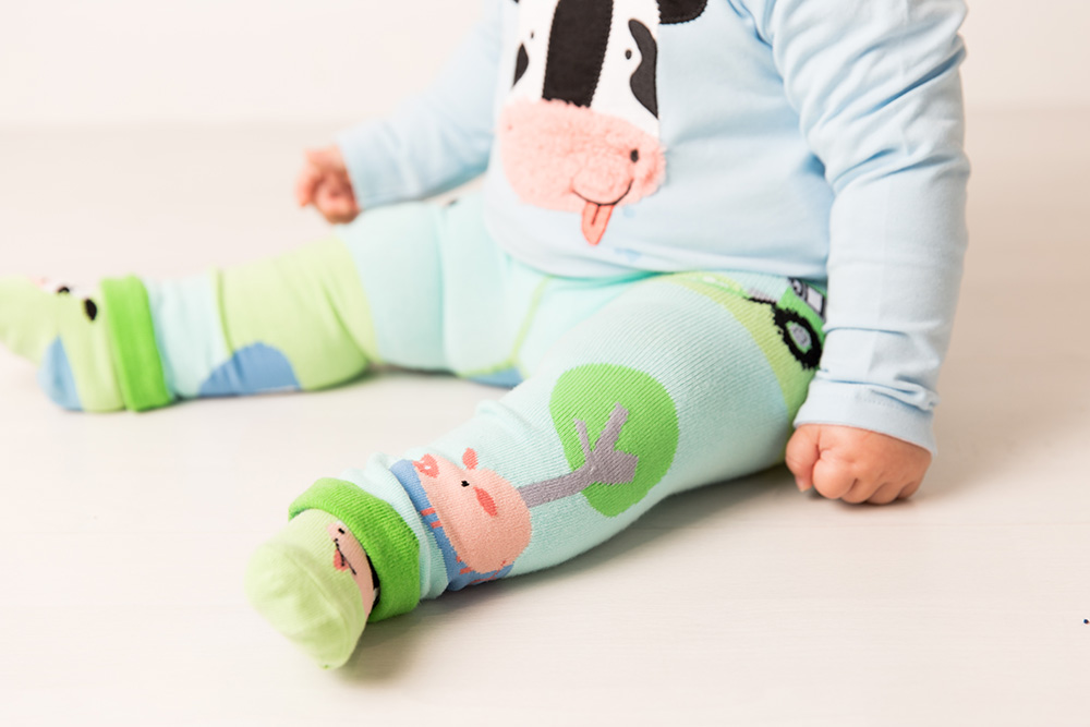 A baby sat on the floor wearing farm themed top and leggings