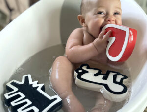 Baby in a bathtub with three Etta Loves x Keith Haring Bath toys