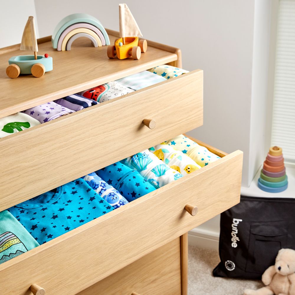 A chest of draws with open drawers full of children's clothes 