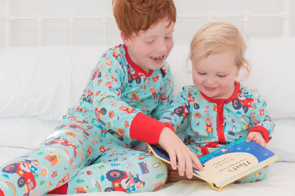 Two children in pyjamas sat reading a book 