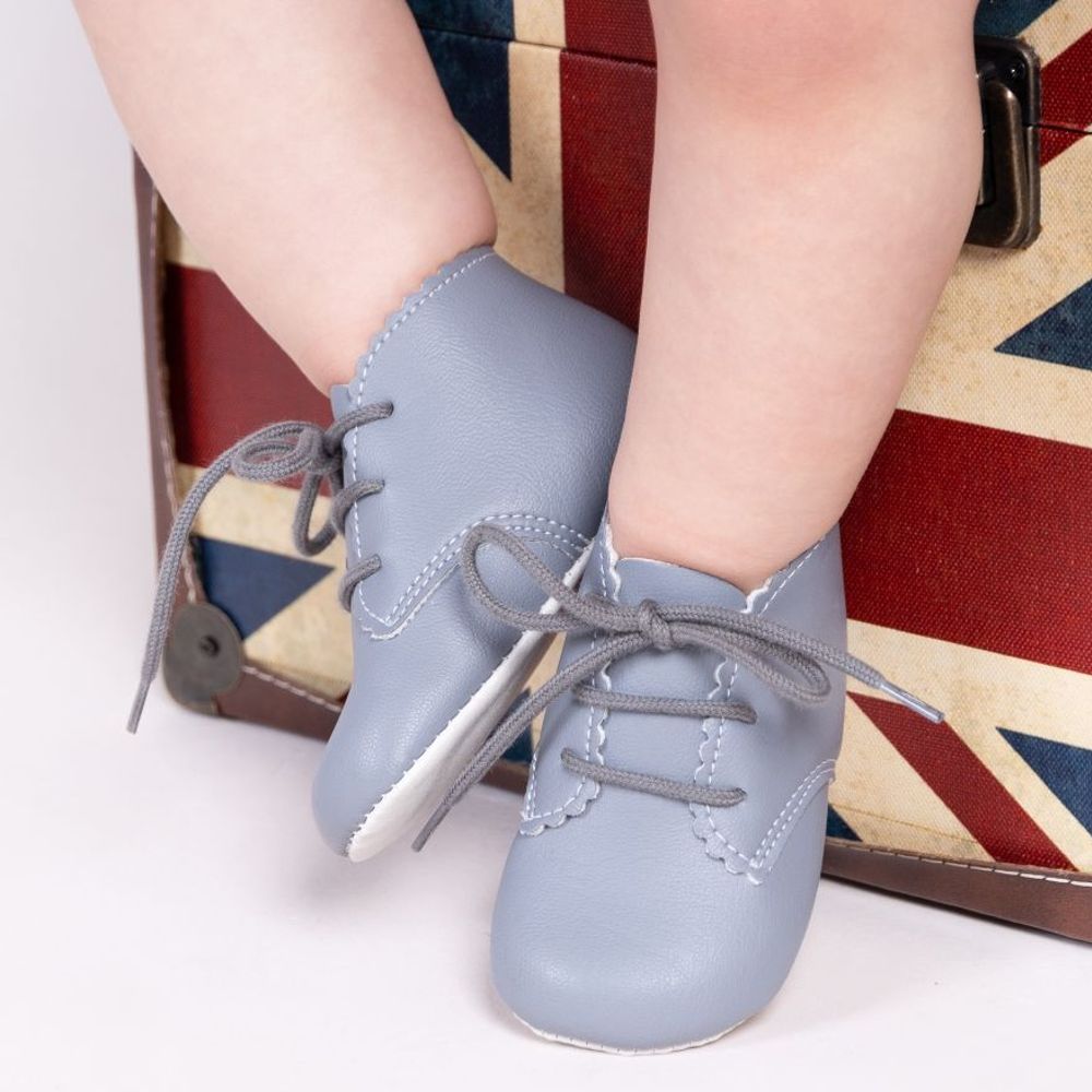 A child's legs in front of a union jack box wearing pale blue lace-up shoes 