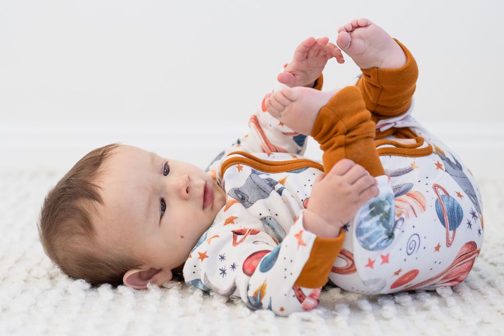 A baby lying on its back wearing planet and stars print sleepwear 