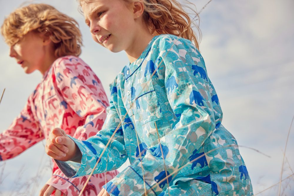 Two children in pink and blue pyjamas running in a field 
