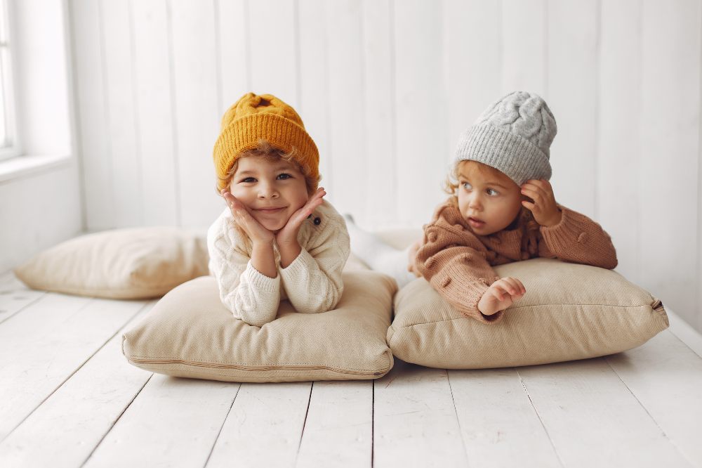 Two young children in hats lying on cushions on the floor