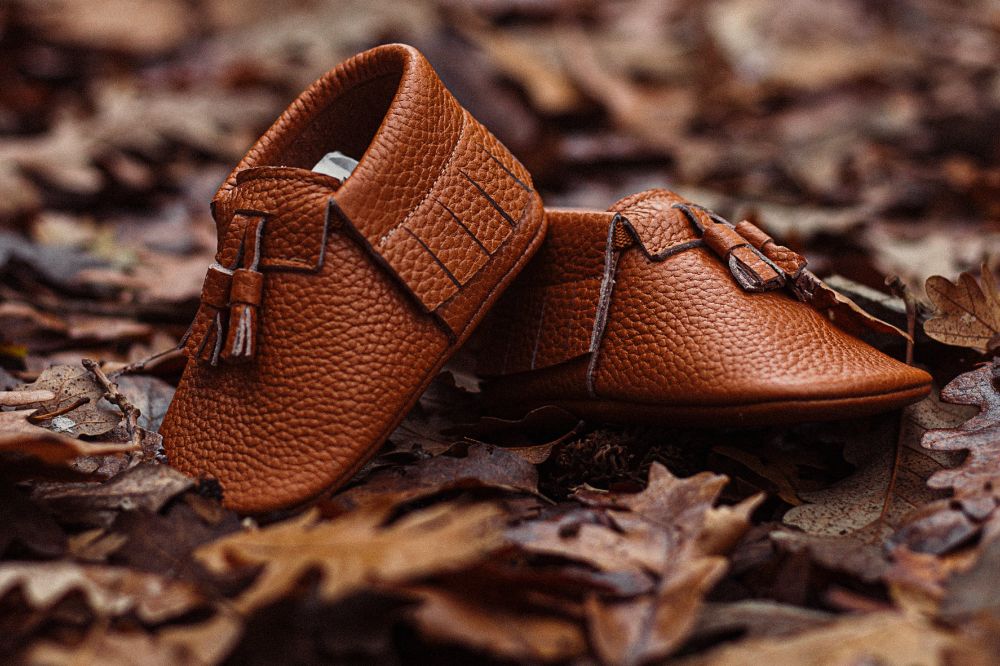 A pair of brown leather baby shoes on a floor of leaves