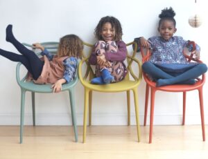 Three children on coloured chairs laughing wearing outfits by Pigeon