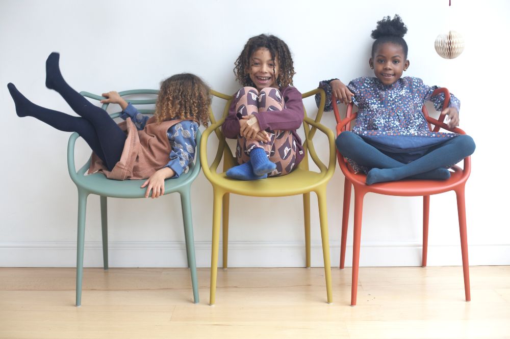 Three children on coloured chairs laughing wearing outfits by Pigeon