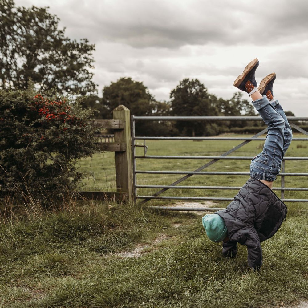 A boy doing a handstand in a field in front of a gate