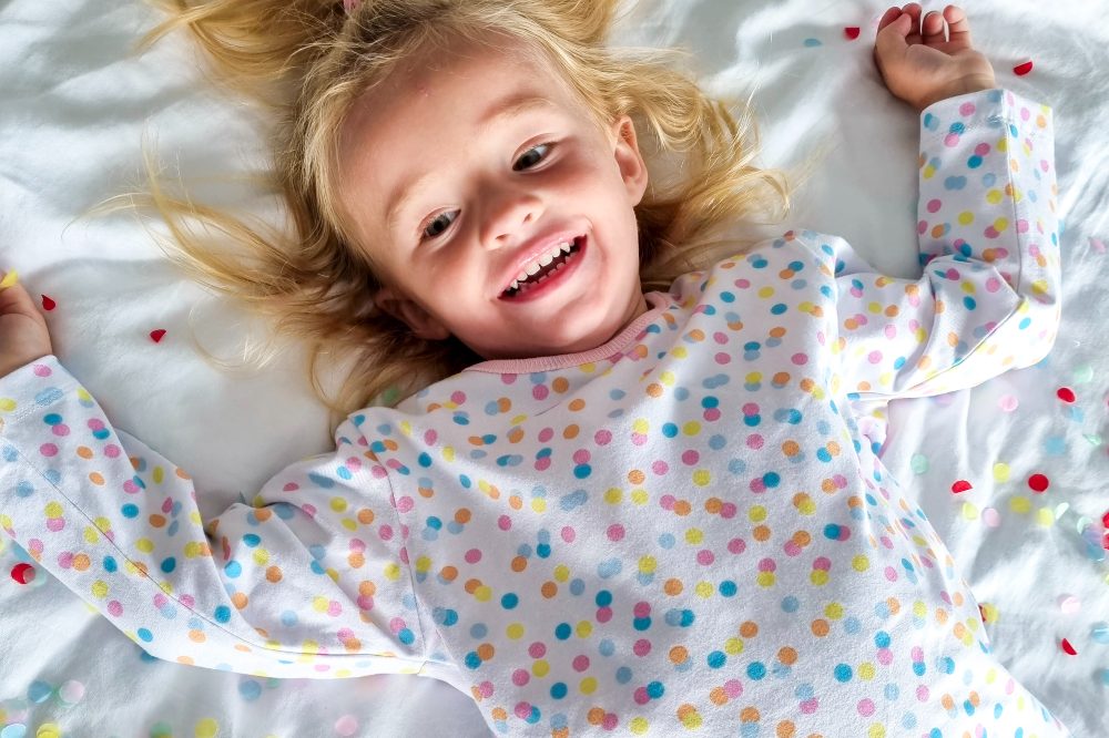 A child lying on a bed wearing spotty pyjamas 