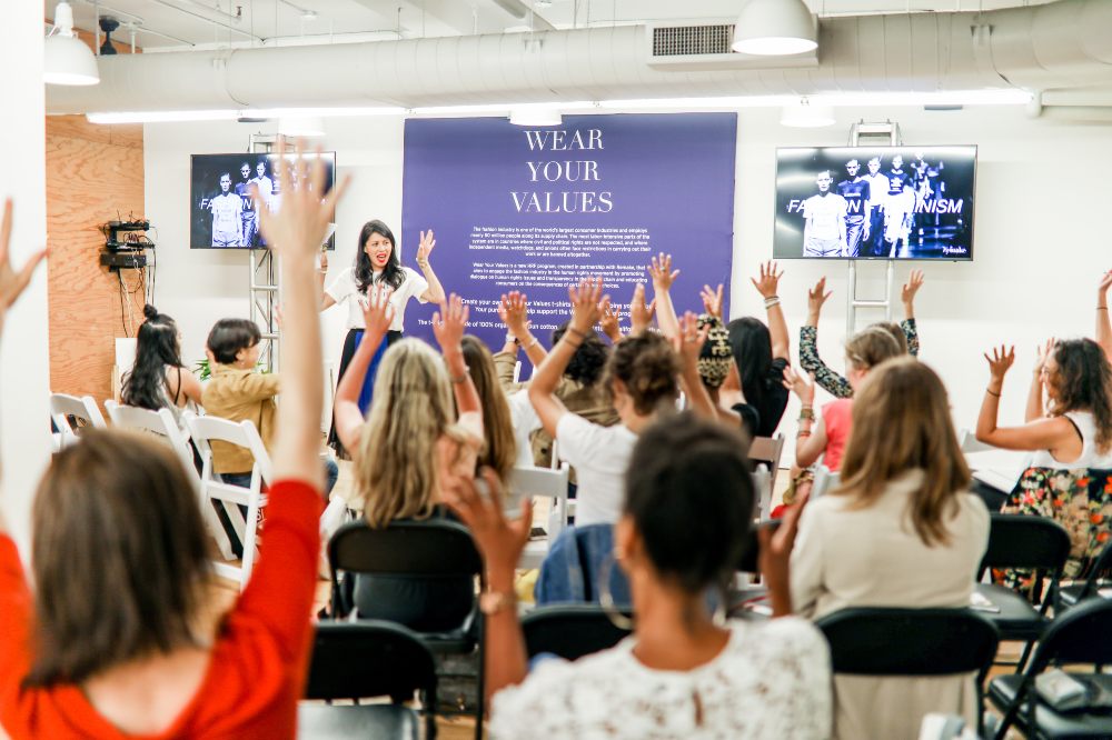 A group of people sat in a room for a Remake event raising their arms