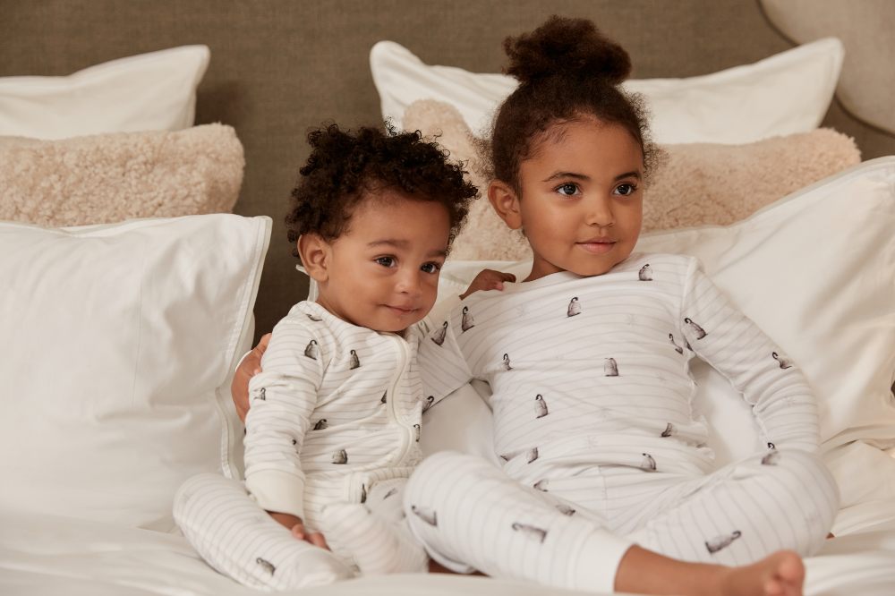 Two young children sat on a bed in sleepwear 