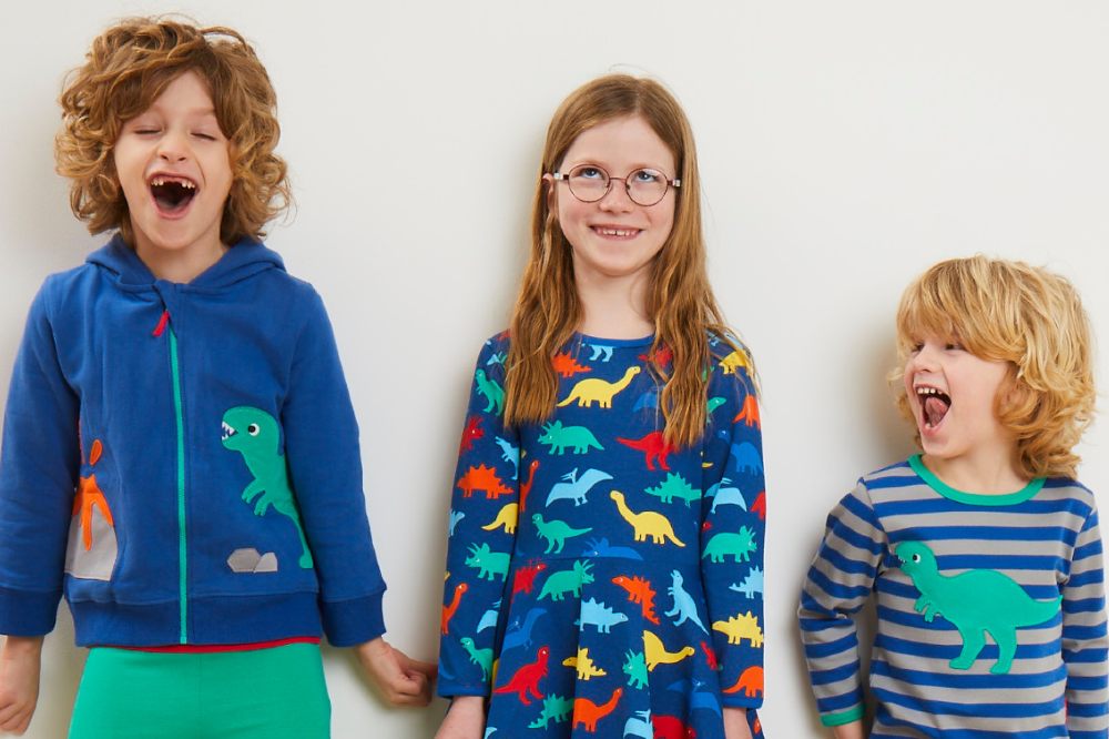 Three children stood against a white wall wearing dinosaur print outfits by Toby Tiger