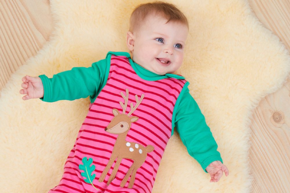 A baby lying on a sheepskin rug wearing a babygro with a deer on the front by Toby Tiger 