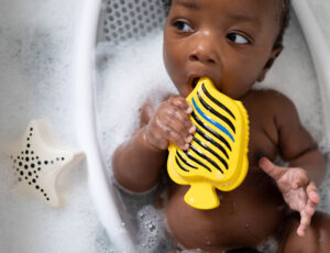 A baby sat in a bath tub holding a yellow and black striped bath toy