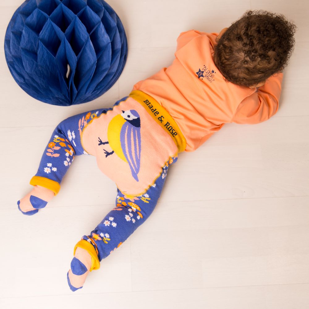 A baby lying on the floor wearing an orange top and leggings with a bird on the bottom