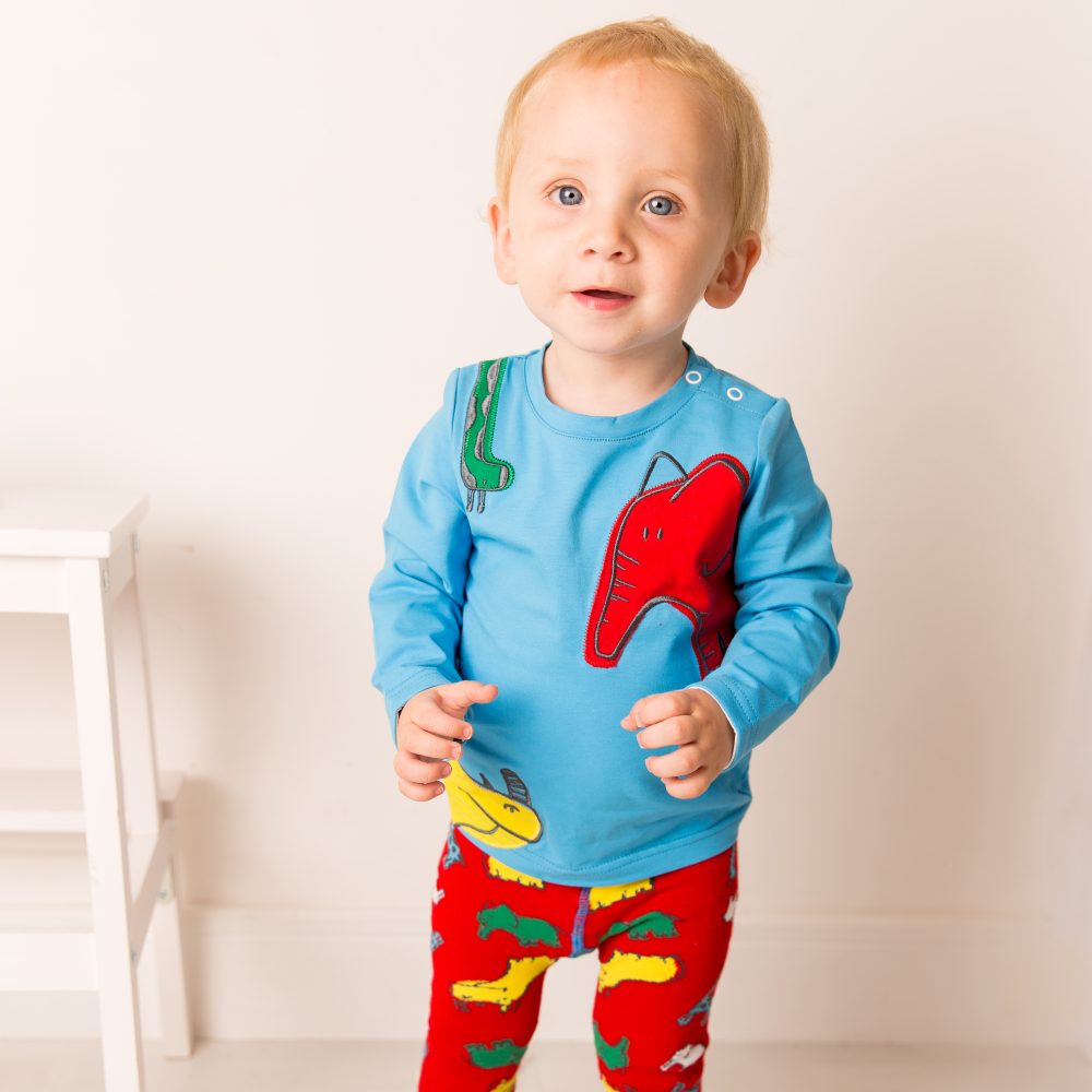 A baby wearing a blue top and red leggings with animals on them 