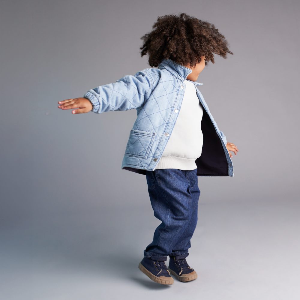 A young child wearing a denim quilted jacket and jeans by KIDLY