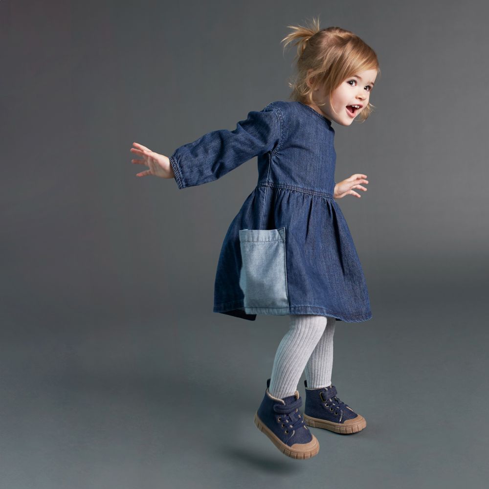 A young girl jumping up wearing a denim dress