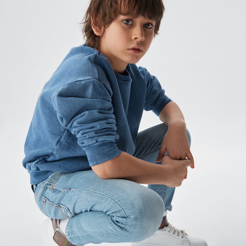 A boy knelt down wearing a blue sweatshirt and jeans 