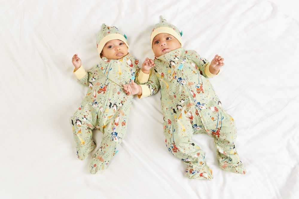 Two babies lying on their backs wearing hats and sleepsuits by Luca and Rosa