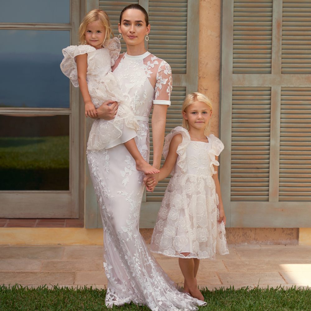 A woman and two young children wearing matching white ocassionwear dresses 