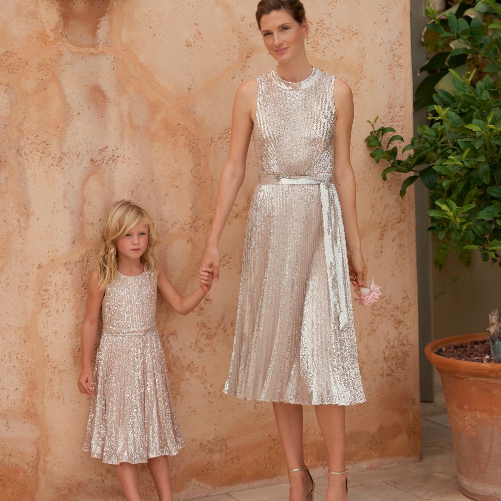 A woman and child holding hands wearing matching silver dresses 