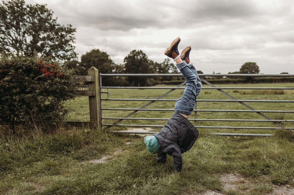A child doing a handstand in a field in front of a gate 