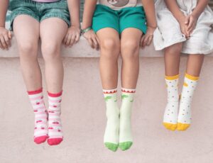 Three children sat on a wall wearing socks by Rockahula Kids