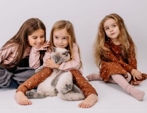Three girls sat on the floor holding a grey and white cat