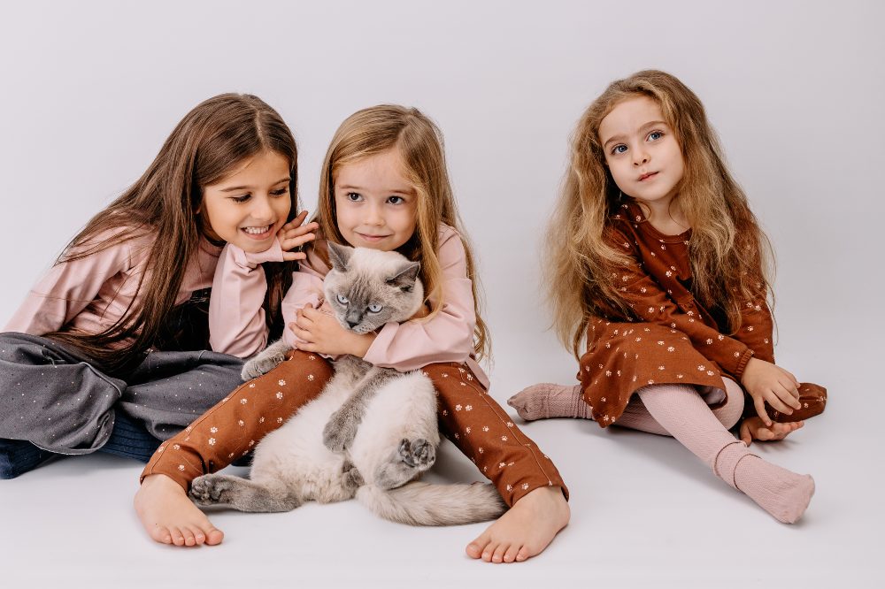 Three girls sat on the floor holding a grey and white cat