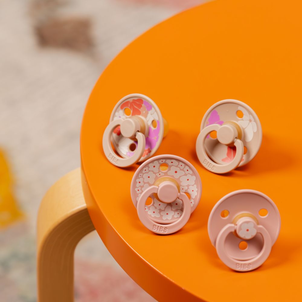 Pink floral print baby pacifiers displayed on a yellow table